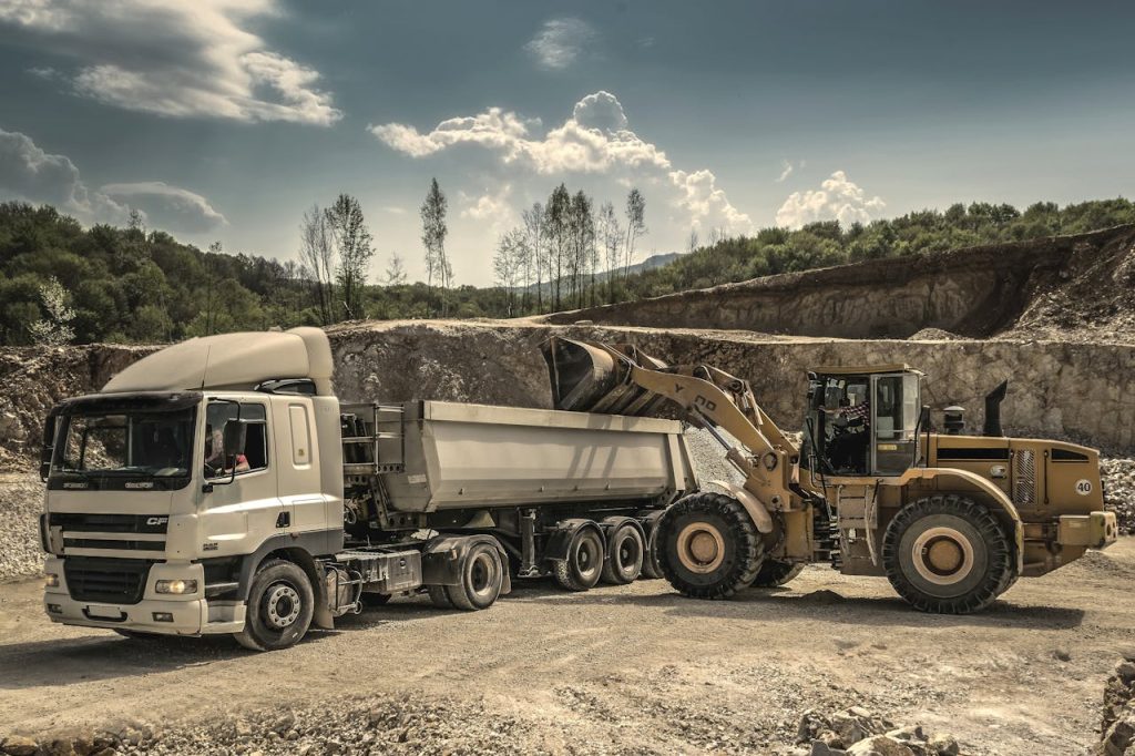 front-load-loader-beside-white-dump-truck-188679 Excavator and truck working together in a quarry, showcasing industrial equipment and operations.